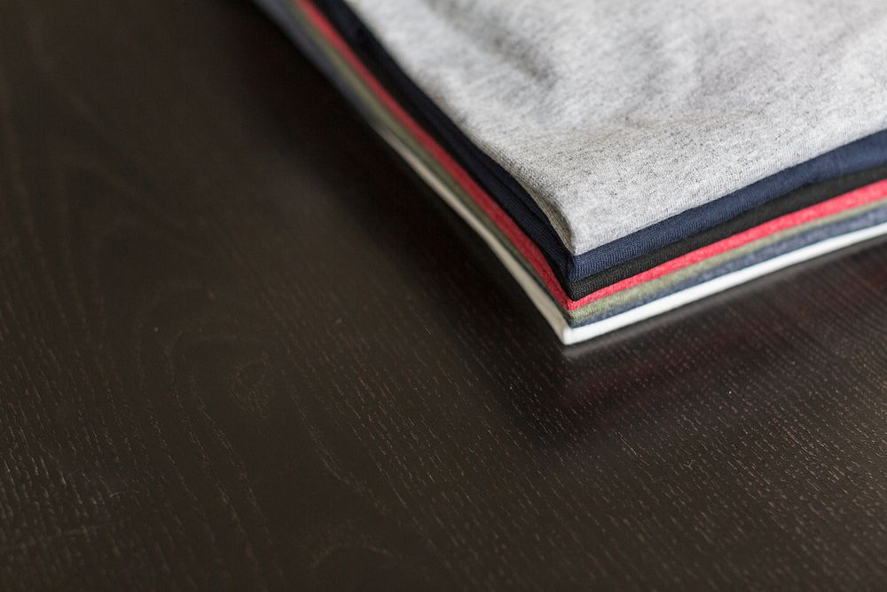 Stack of 7 folded plain t-shirts on table.