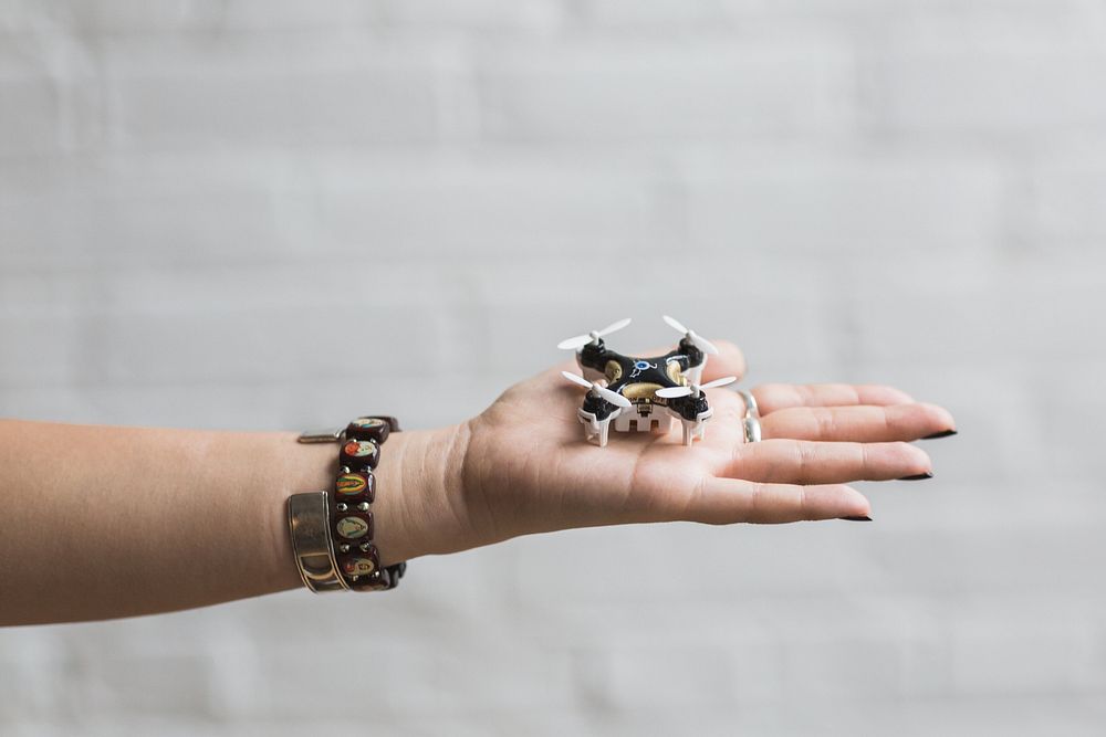 White, black, and gold drone in the palm of a womans hand.