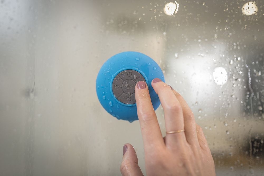 Woman pressing grey button on blue speaker on shower glass.
