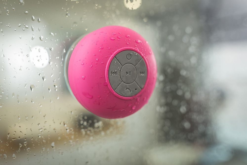 Pink waterproof speaker on shower glass.