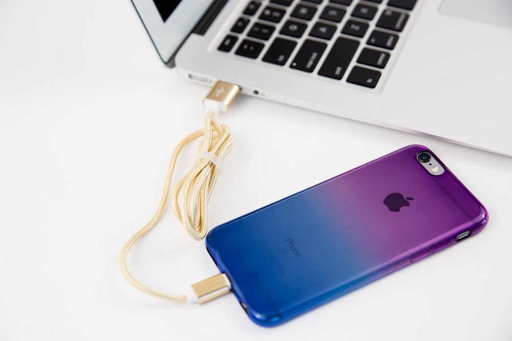 Apple iPhone MacBook with gold charging cable and iPhone.
