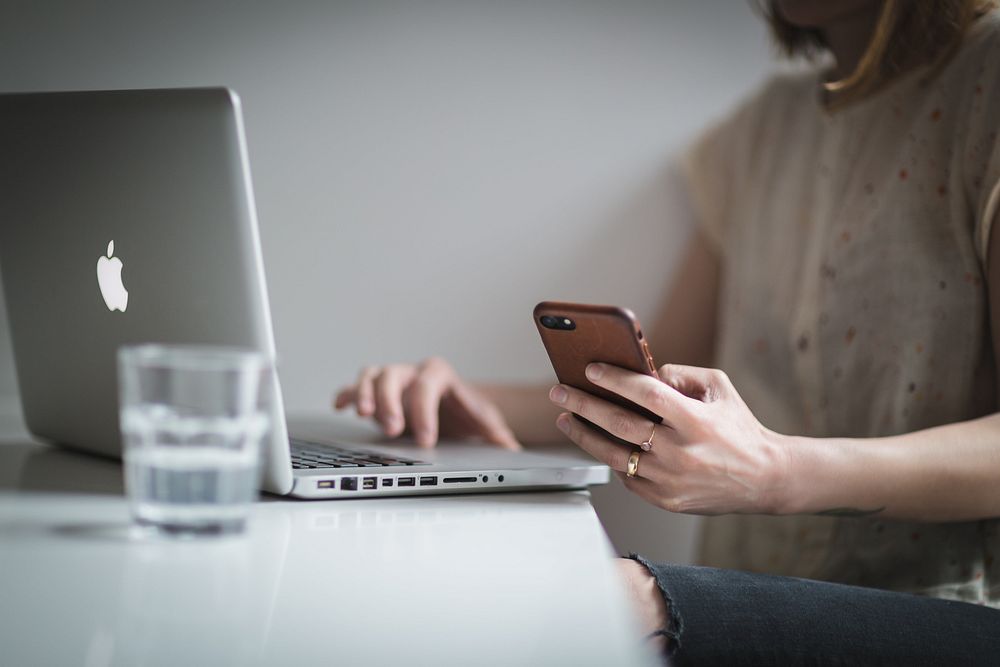 Woman checking cell phone while working on laptop.