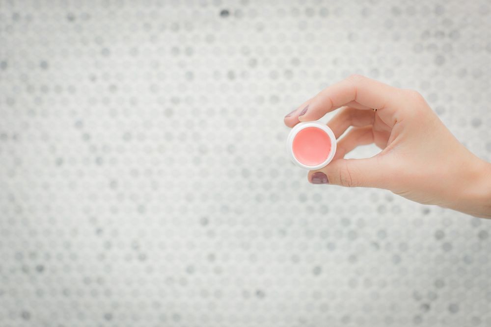 Woman holding container of homemade lip balm with her fingers.