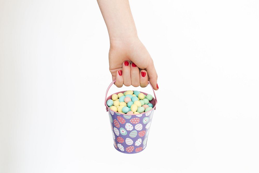 A woman's manicured hand holds a small Easter egg hunt basket that is full of mini chocolate eggs.