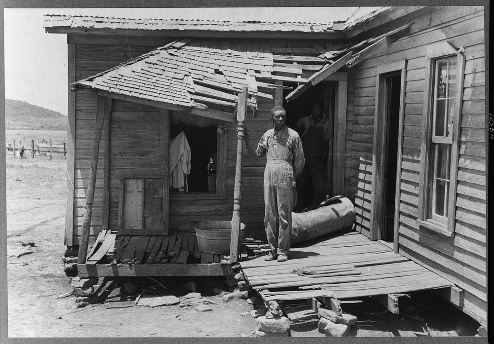 tenant farmer on his front porch. This farm is owned by an out-of-state woman and has been rented by this family of Negroes…