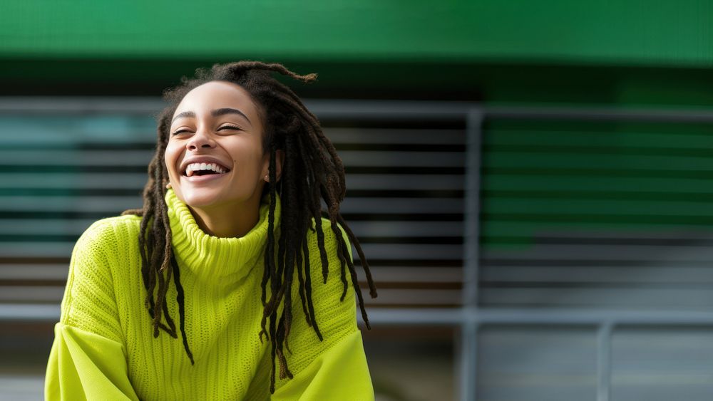 a woman with dreadlocks smiling wearing lime green sweater, playful poses, close up, outdoor city, cool.  