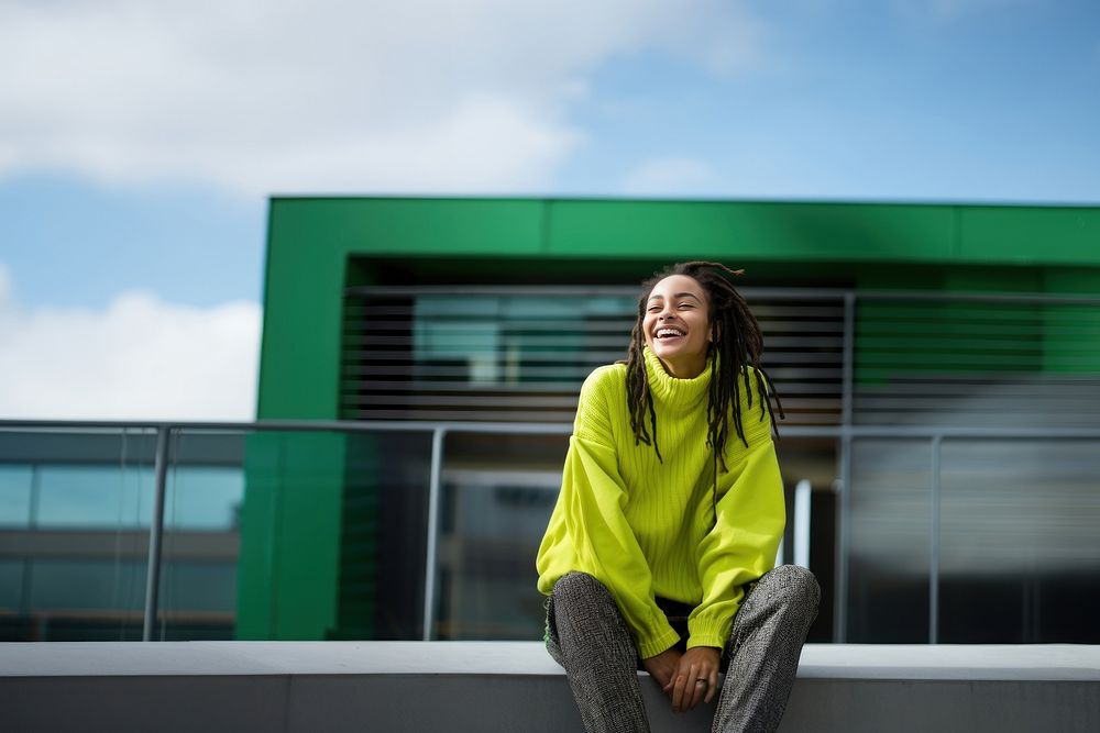 a woman with dreadlocks smiling wearing lime green sweater, playful poses, close up, outdoor city, cool.  