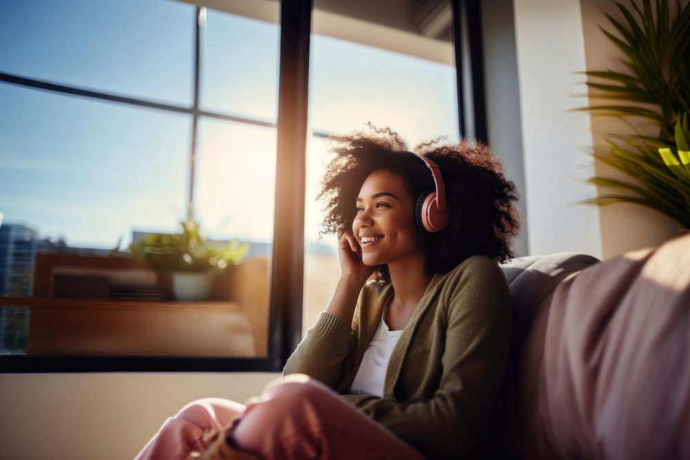 photo of A black woman sitting on a couch happy with wearing headphones in a minimal living room. 