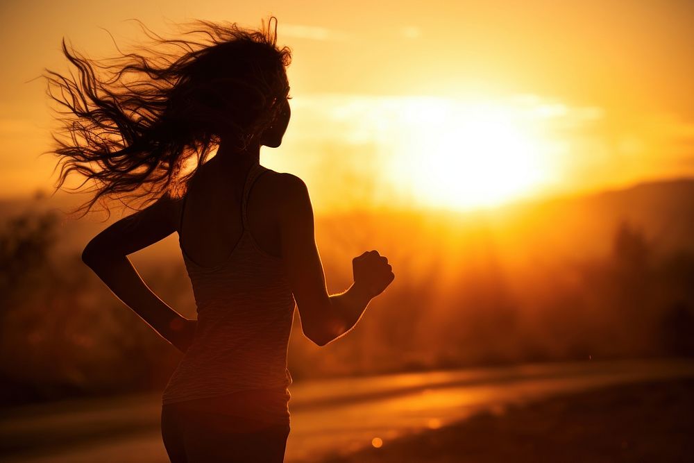 Young woman running against morning sun backlighting adult silhouette. 