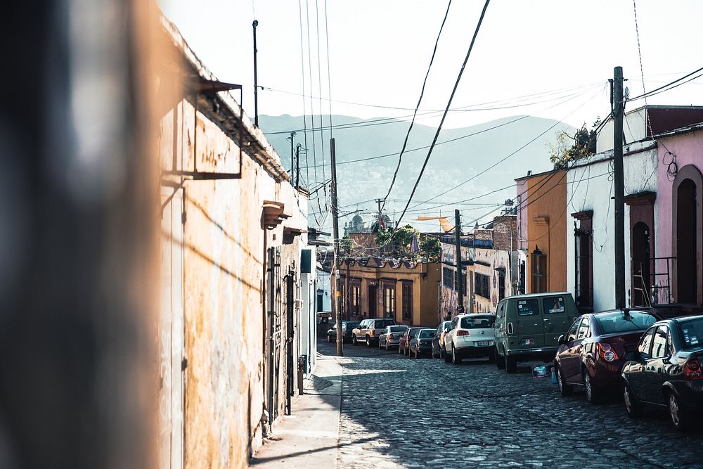 Cobblestone road lined with cars in a mountain town. The mountains are beckoning in the distance.