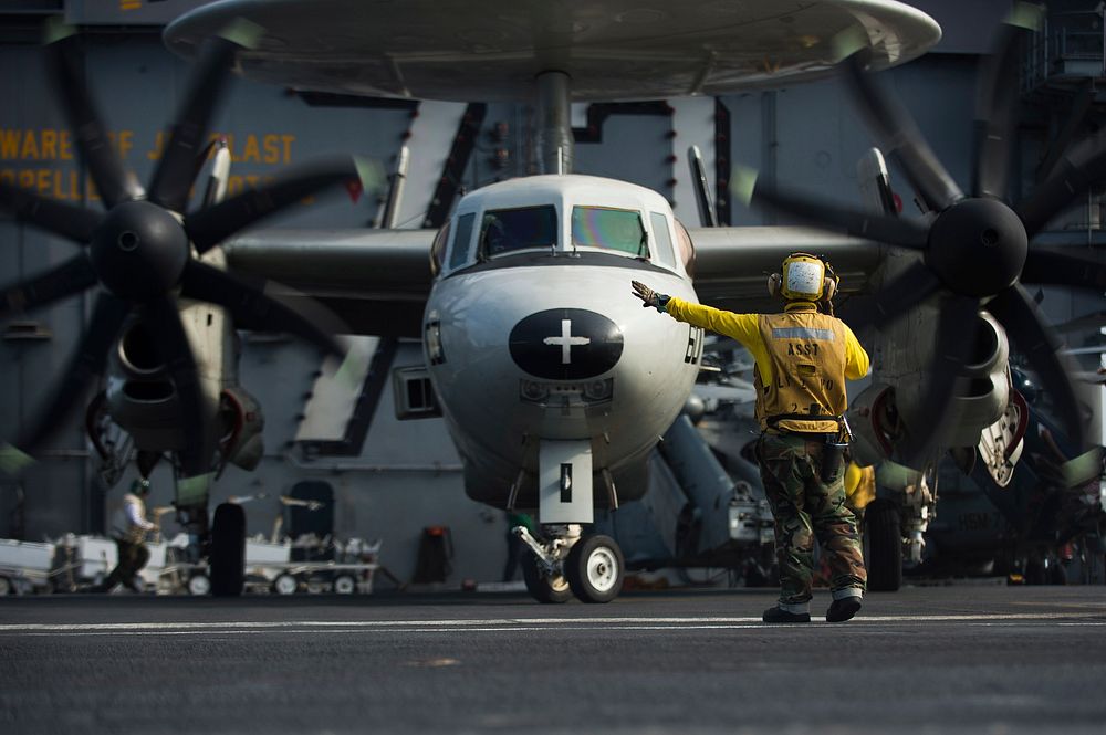 U.S. Navy Boatswain's Mate (Handling) 3rd Class Adrian Ramilo directs the pilots of an E-2C Hawkeye aircraft assigned to…
