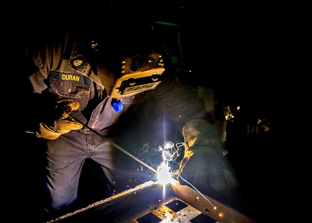 U.S. Navy Chief Damage Controlman Rodney Duran welds a steel bar aboard the guided missile destroyer USS Donald Cook (DDG…