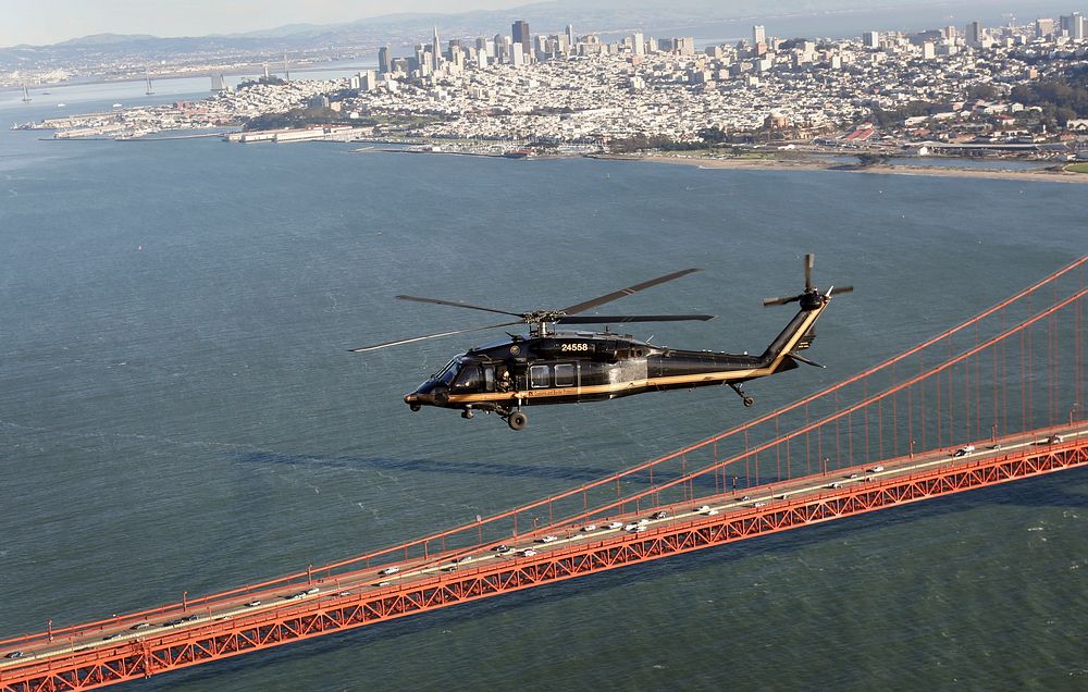 A U.S. Customs and Border Protection Black Hawk helicopter flies over the Golden Gate Bridge with San Francisco in the…