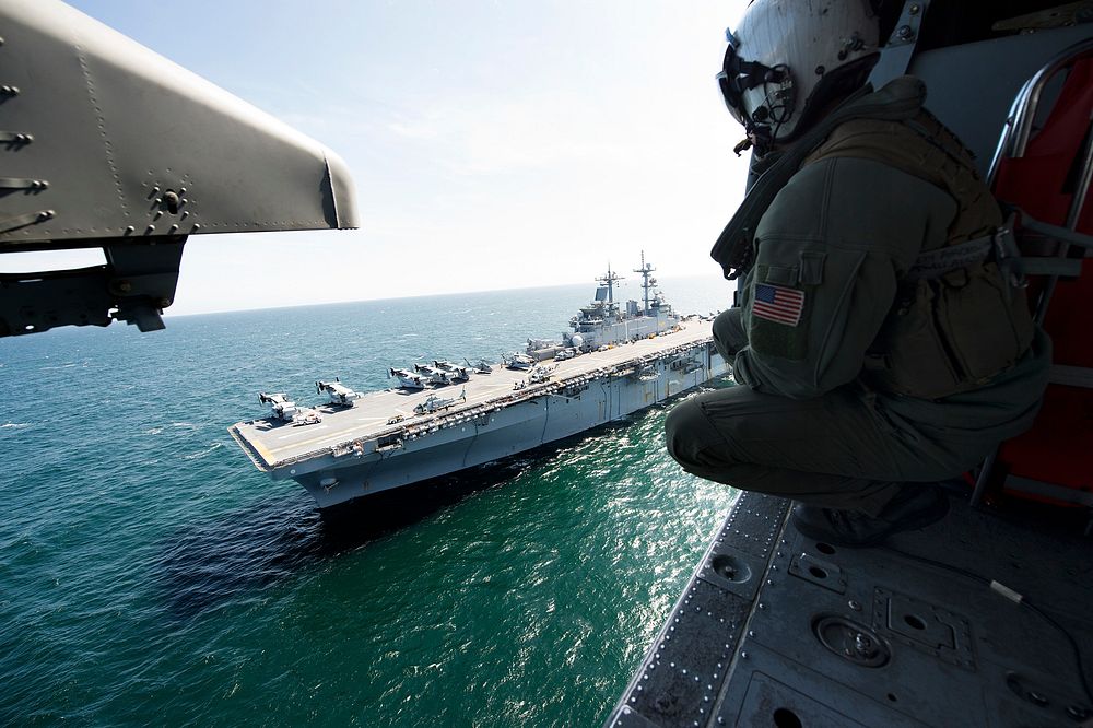 A U.S. Sailor looks out at the amphibious assault ship USS Wasp (LHD 1) from an MH-60S Seahawk helicopter over the Atlantic…