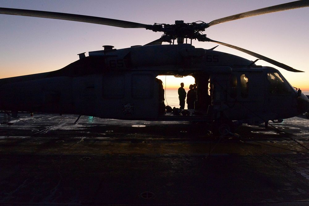 U.S. Sailors assigned to the Blackjacks of Helicopter Sea Combat Squadron (HSC) 21 observe the sun rise next to an MH-60S…