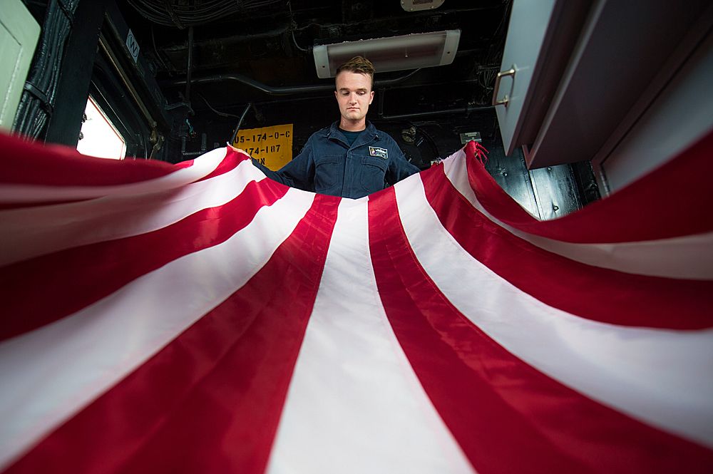 U.S. Navy Quartermaster 3rd Class Scott Farrell folds the national ensign aboard the guided-missile cruiser USS…