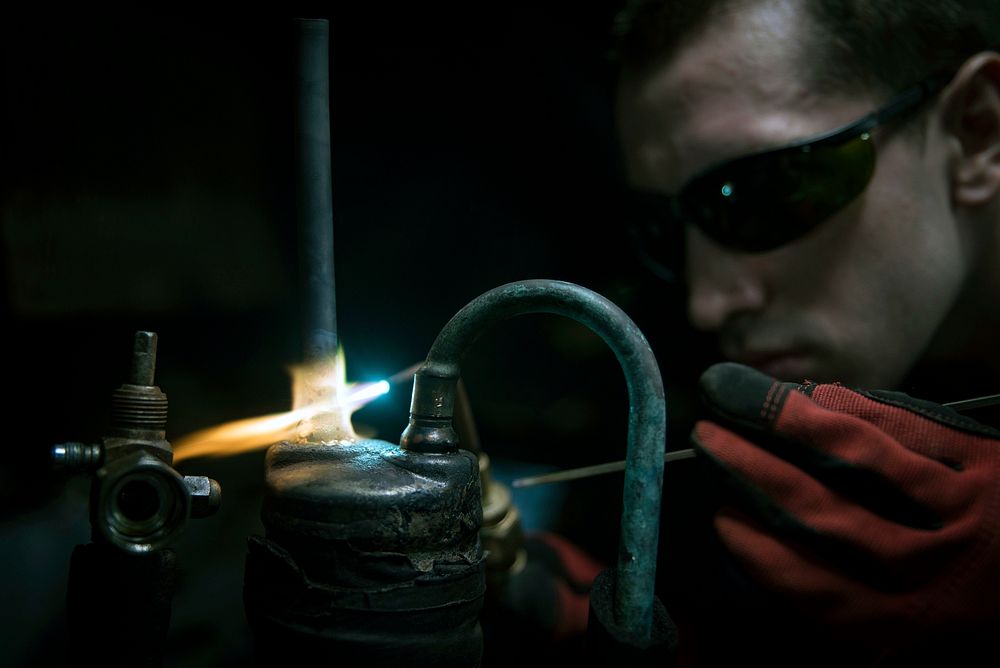 U.S. Navy Hull Maintenance Technician 2nd Class Anthony McGinley brazes a filter unit in the pipe shop of the aircraft…