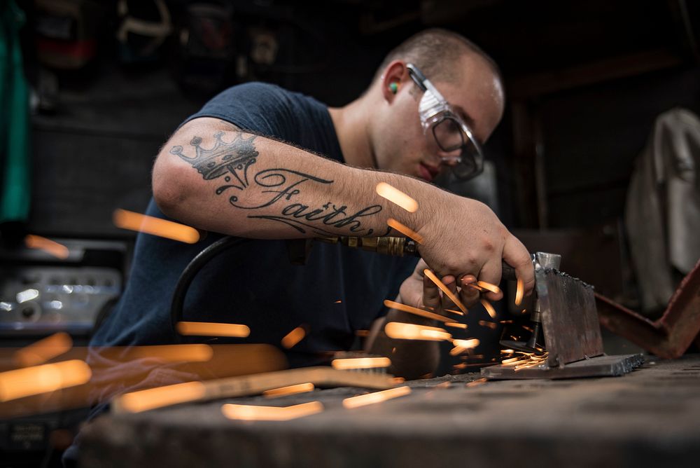 U.S. Navy Hull Maintenance Technician 3rd Class Cullen Kyser, from Youngstown, Ohio, grinds metal for a pneumatic grinder…