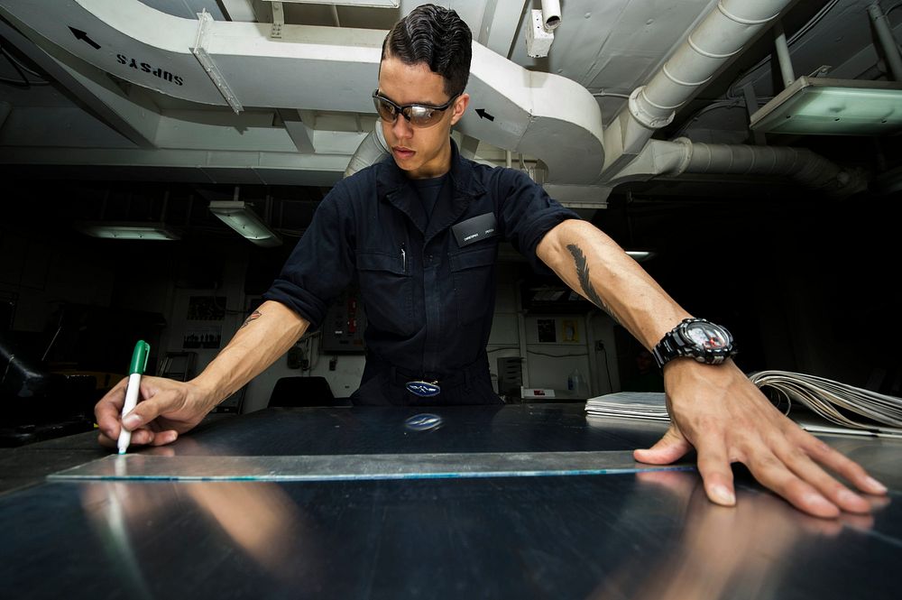 U.S. Navy Seaman Christopher Jackson, from Port St. Lucie, Florida, uses a marker to outine where to cut on sheet metal…