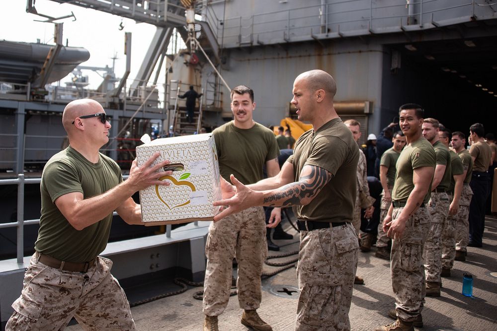 U.S. Marine Corps 1st Lt. Brock Yackey, left, a combat engineer officer with the 22nd Marine Expeditionary Unit, hands a box…
