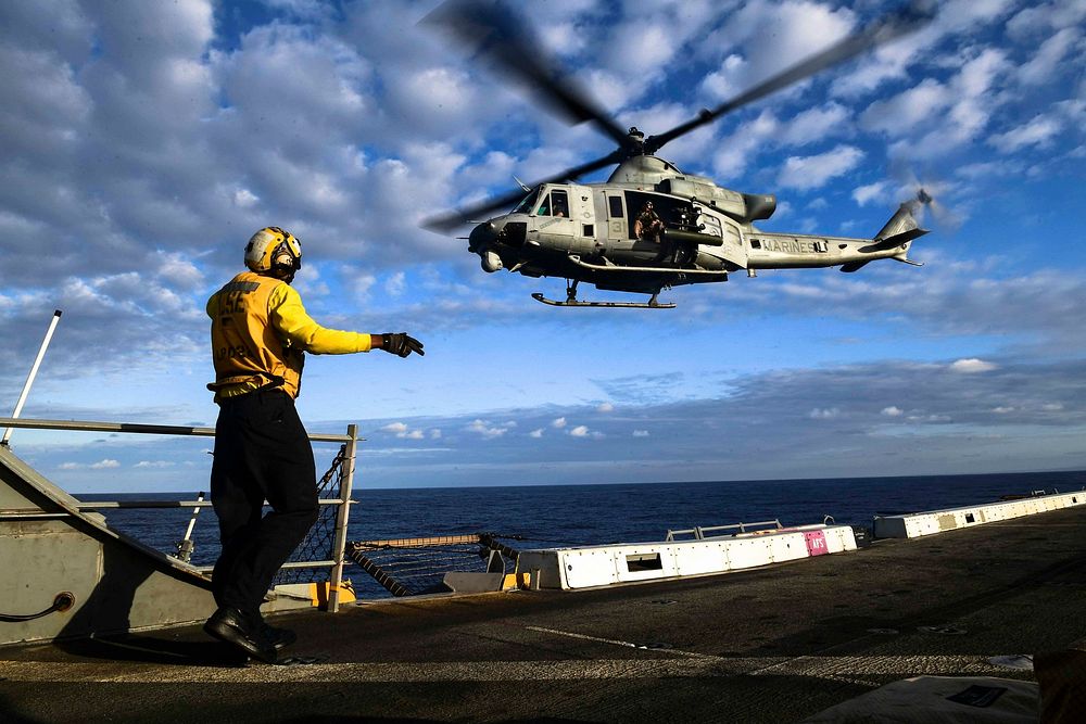 U.S. Navy Aviation Boatswain’s Mate (Handling) Airman Anthony Similton signals a UH-1Y Venom helicopter assigned to Marine…
