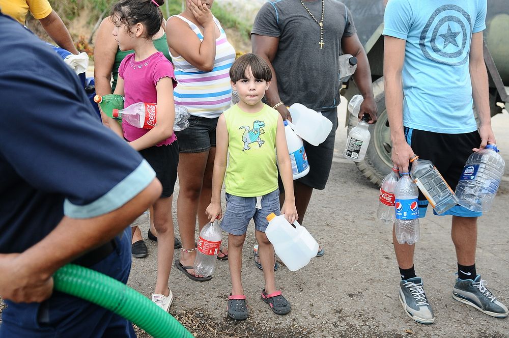 A boy waits for water distributed by U.S. Soldiers with the Puerto Rico National Guard, along with employees from the…