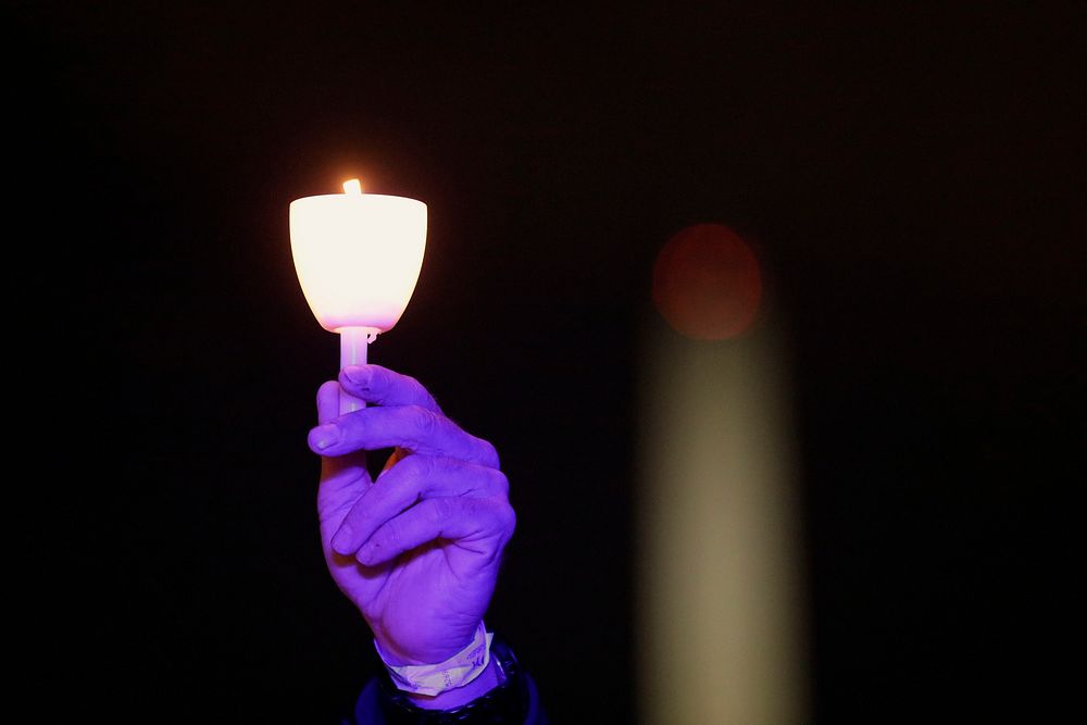 A candle is held high against the backdrop of the Washington Monument at the conclusion of the 31st Annual Candlelight Vigil…