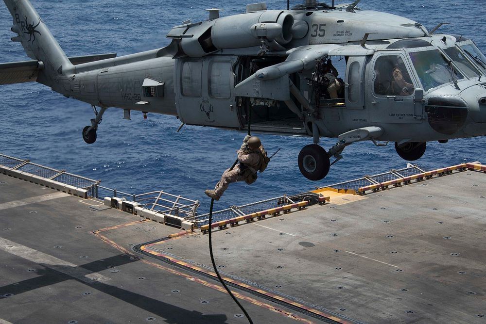 A U.S. Marine assigned to the 26th Marine Expeditionary Unit, fast ropes from an MH-60S Sea Hawk helicopter attached to…