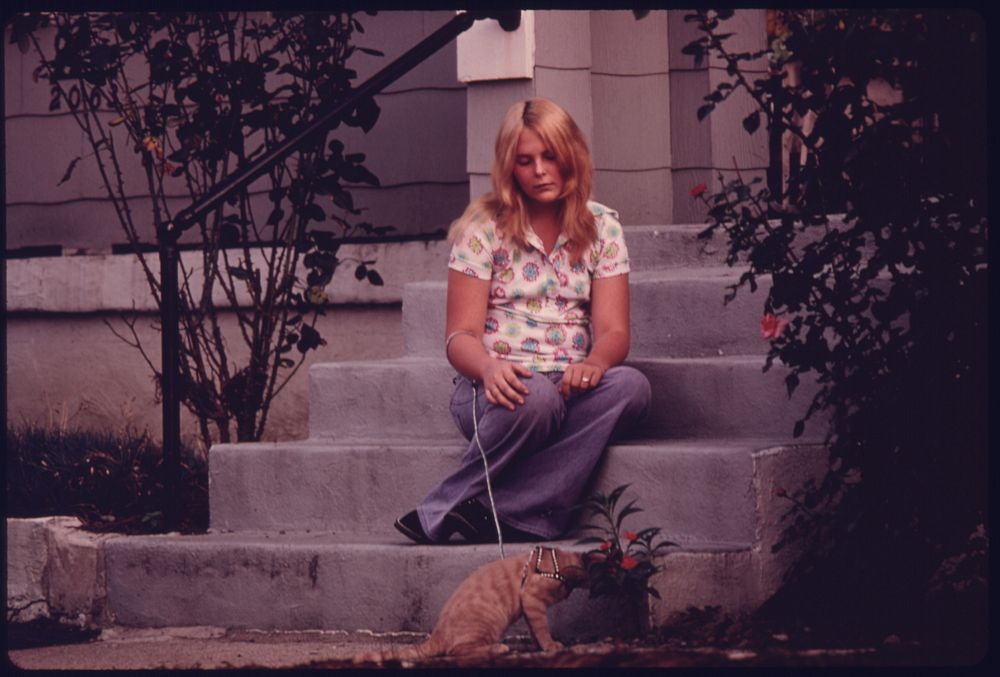 Young Girl Sits on the Porch Steps Daydreaming While Her Cat Sniffs Flowers.