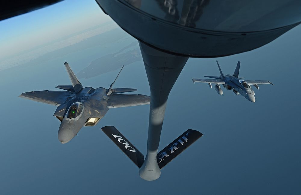A U.S. Air Force F-22 Raptor and a Finnish air force F/A-18 Hornet fly behind a U.S. Air Force KC-135 Stratotanker during…