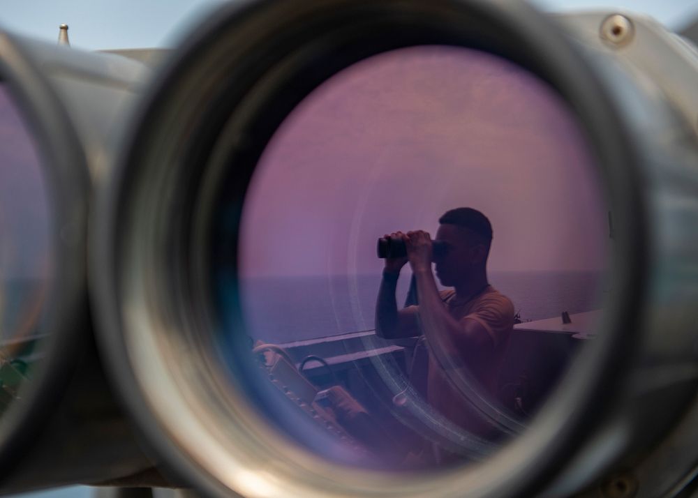 U.S. Navy Culinary Specialist 2nd Class Adrian Bradford uses binoculars to scan the ocean during a bridge watch aboard the…