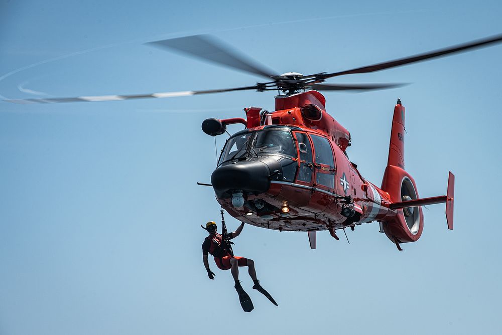 A U.S. Coast Guard (USCG) rescue swimmer hangs of the side of an MH-65 Dolphin off the coast of Tybee Island Coast Guard…