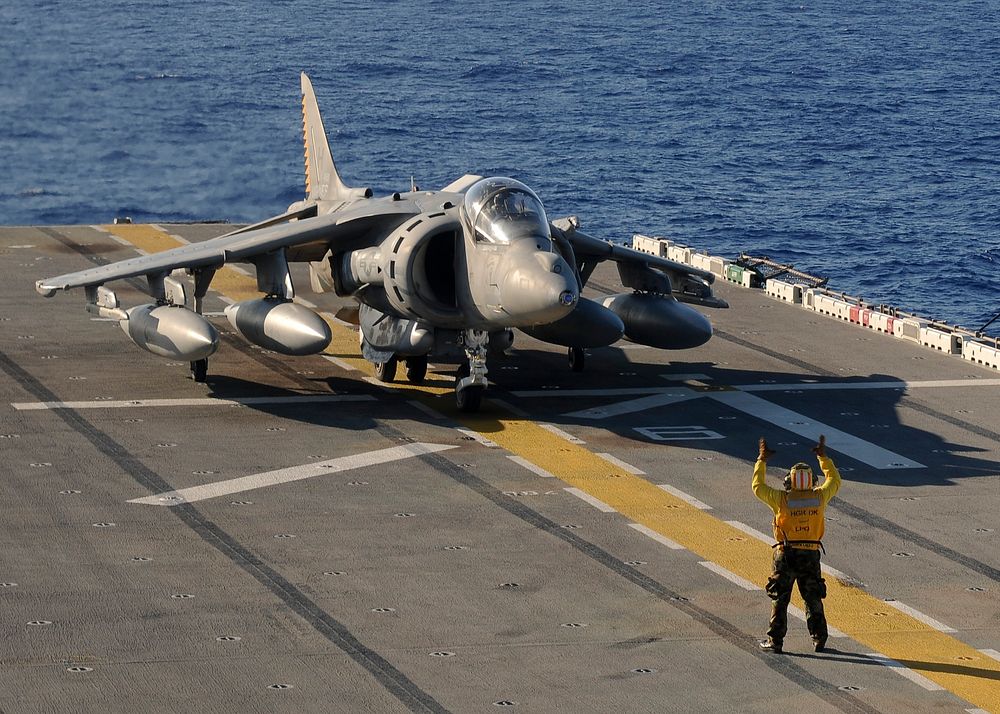 U.S. Navy Aviation Boatswain's Mate 1st Class Michael Quintos directs an AV-8B Harrier jet aircraft as it taxies on the…