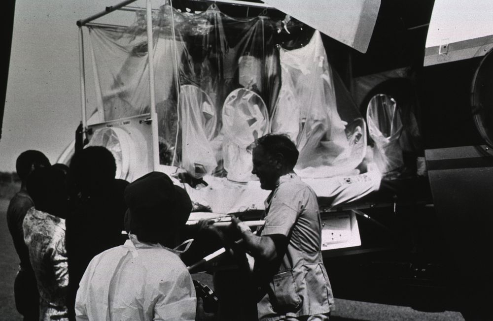 CDC worker exposed to Ebola virus. Several people load a patient enclosed in a plastic bubble into an airplane. Original…