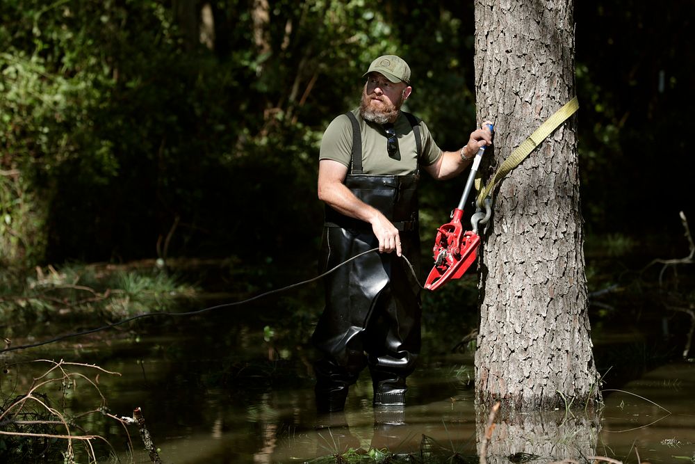 A U.S. Border Patrol agent mans a winch tied to a tree needing removal due to softened soil from flooding associated with…