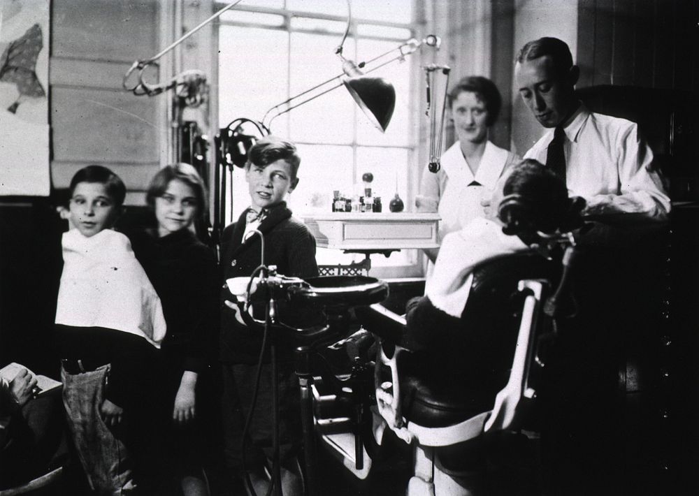 Dental Clinic. View of a dentist, a nurse, and four children, one of whom is sitting in the dental chair in the office.…