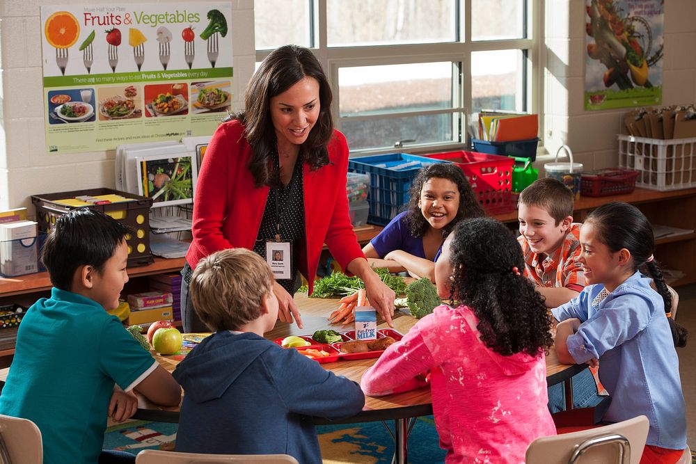 School Nutrition Professional talking with elementary school students about school lunch. Original public domain image from…