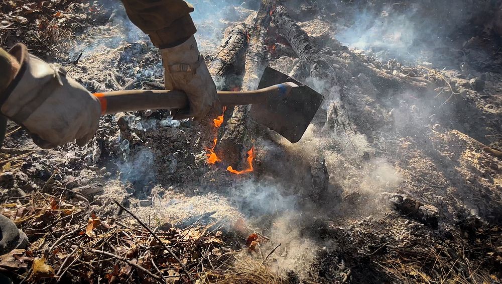 Firefighter tends to a burning pile of brush to ensure that it is fully consumed and contained, during a pile burn to remove…