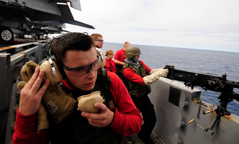 U.S. Navy Aviation Ordnanceman Airman Eric Hornbeck uses a sound-powered telephone near a .50-caliber machine gun mount…