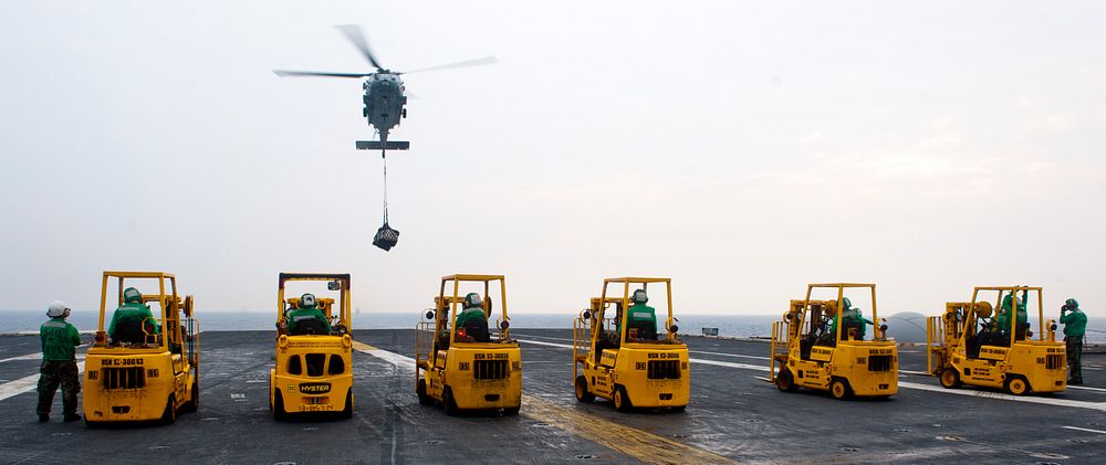 Forklifts line up as an MH-60S Seahawk helicopter attached to Helicopter Sea Combat Squadron (HSC) 8 delivers pallets of…