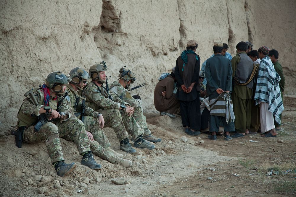 Coalition forces members watch as Afghan Local Policemen and villagers crowd around other coalition forces in Khost village…