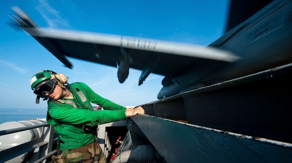 U.S. Navy Aviation Boatswain's Mate Equipment Airman Justin Bryan ducks as an F/A-18E Super Hornet aircraft assigned to…