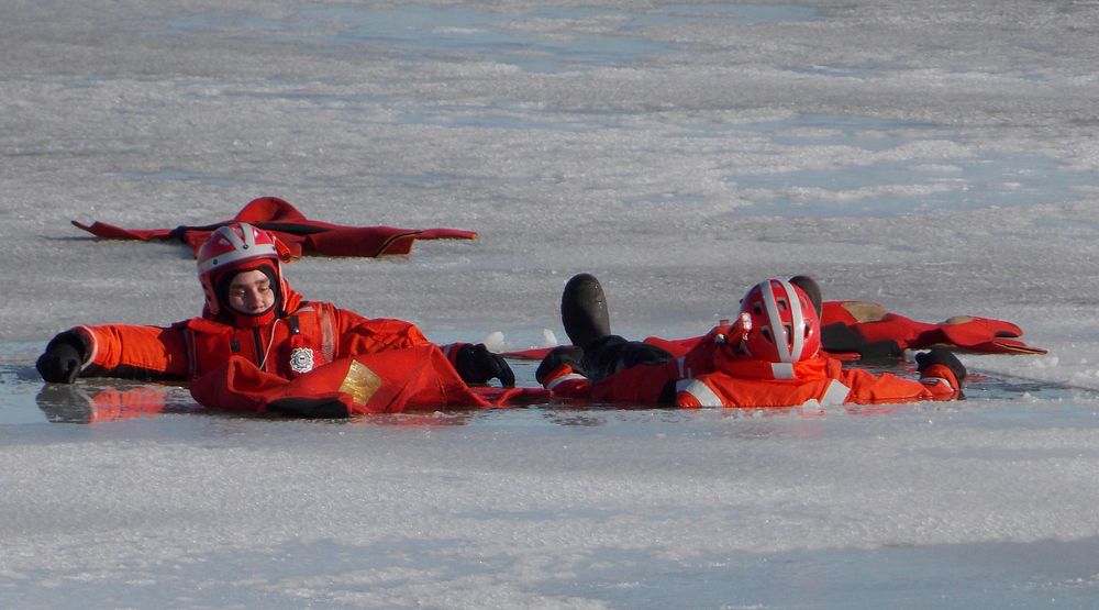 U.S. Coast Guard members acting as simulated victims await rescue in an opening in frozen Lake Erie during the Icy Resolve…