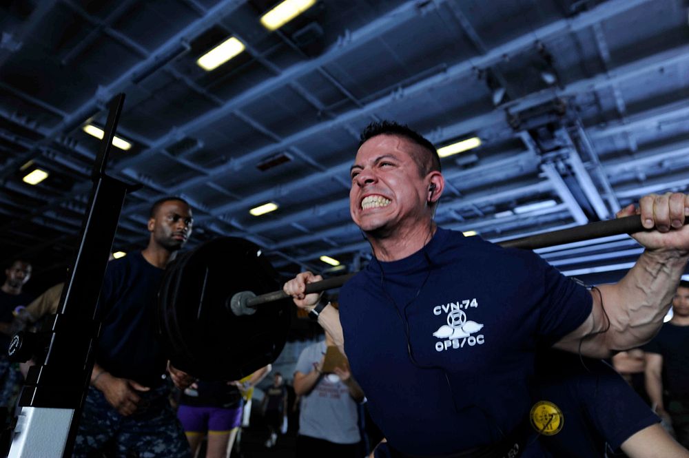 U.S. Navy Air Traffic Controller 1st Class Javier Lopez lifts weights during a squat competition in the hangar bay aboard…