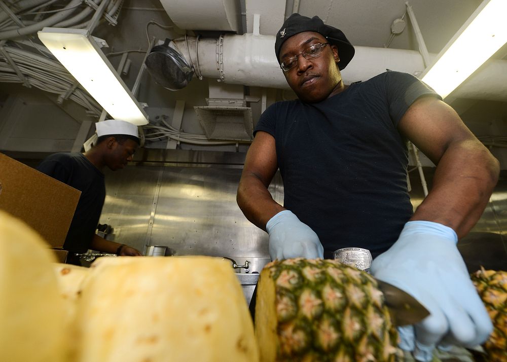 U.S. Navy Culinary Specialist 3rd Class Kenneth Williams slices a pineapple in the galley on the aft mess decks aboard the…