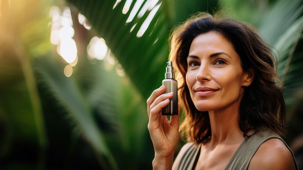 close up face shot photo of a middle aged hispanic woman face holding serum bottle close to her face.  