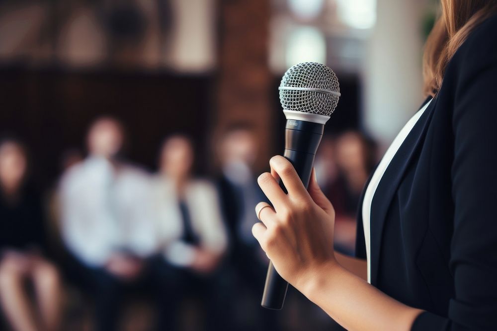 Woman presenter delivering a presentation using mic microphone audience adult. AI generated Image by rawpixel.