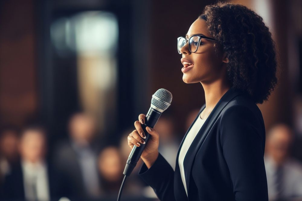 Black woman presenter delivering a presentation using mic microphone audience adult. AI generated Image by rawpixel.