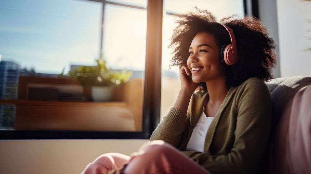 photo of A black woman sitting on a couch happy with wearing headphones in a minimal living room. 