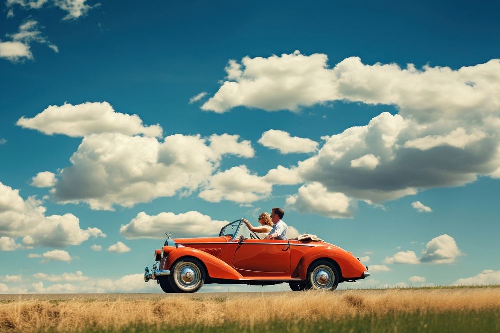 Photo of couple driving in red vintage car on countryside. 